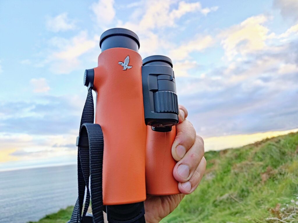 A Swarovski Optik NL Pure 10x32 binocular review featuring a person holding a pair of orange binoculars.