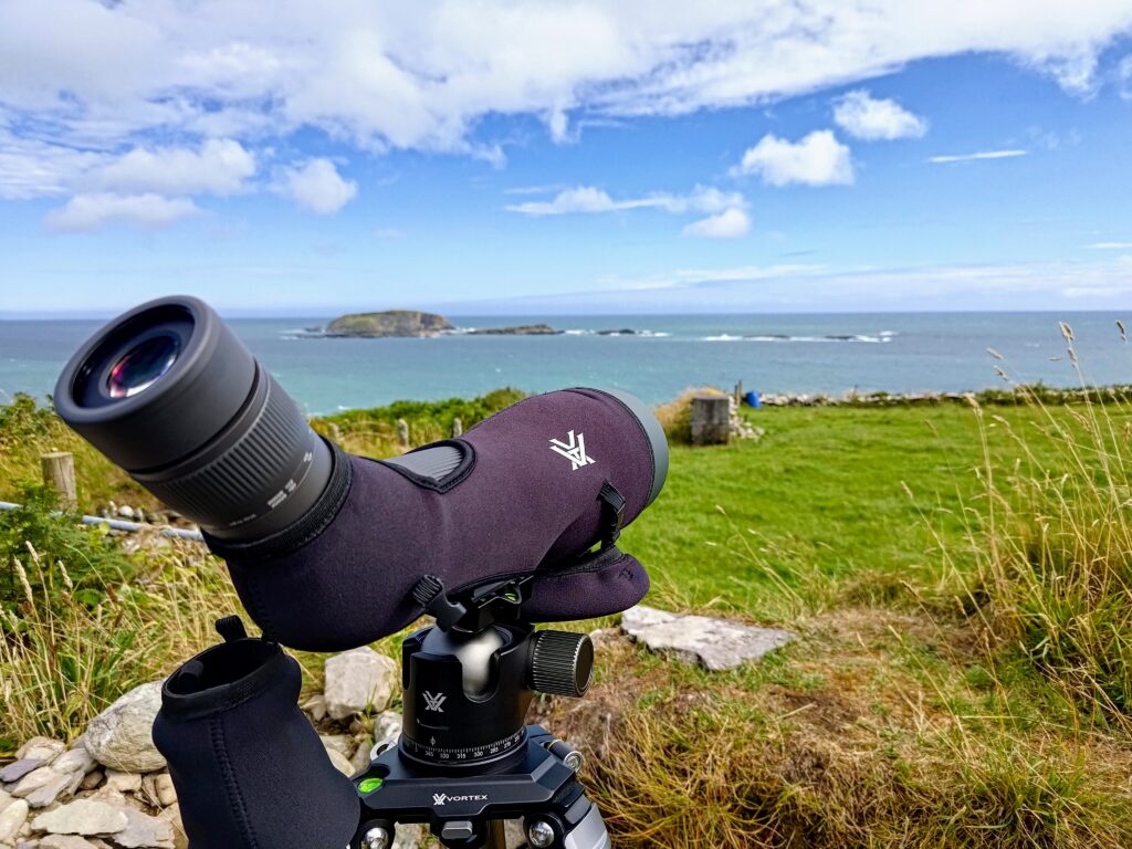 A pair of Vortex binoculars on a tripod with a view of the ocean.