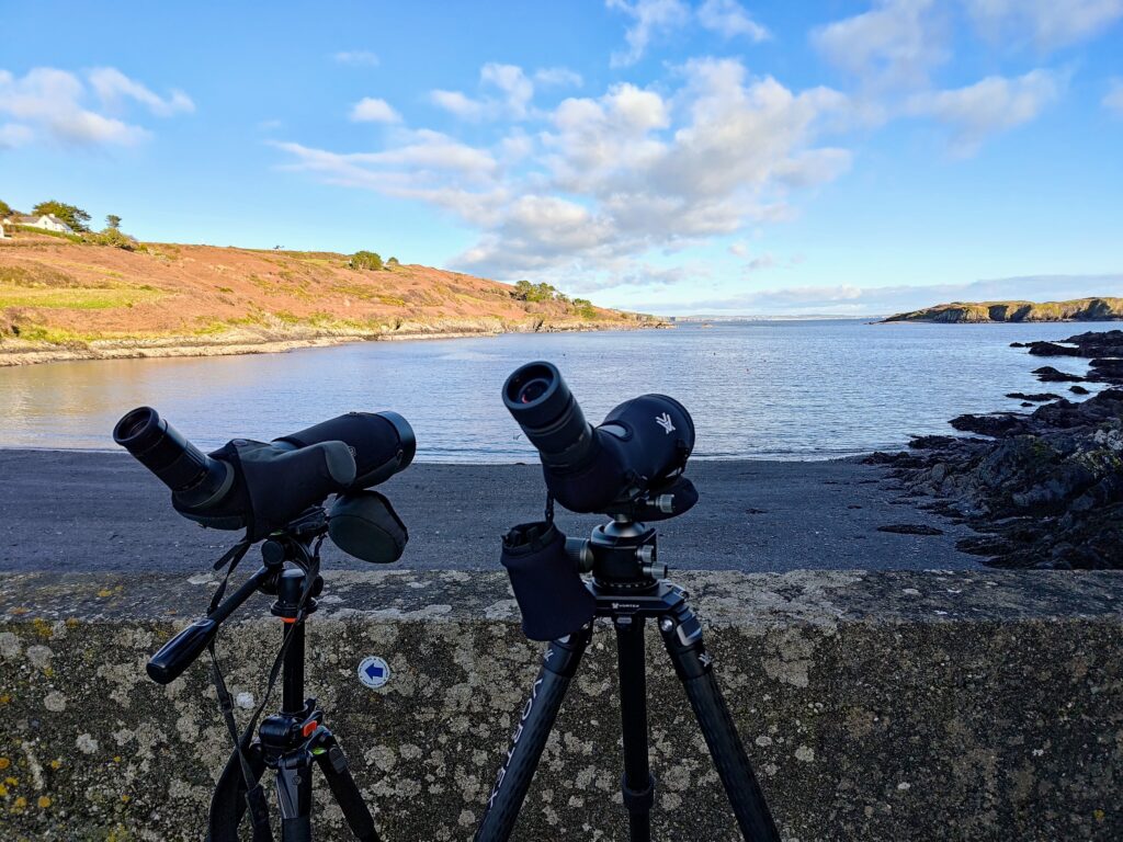 A pair of Vortex binoculars on a tripod next to a body of water.